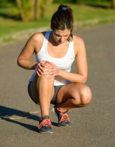 Coureuse accroupie se tenant le genou, gênée par une douleur au tendon pendant une sortie de course à pied