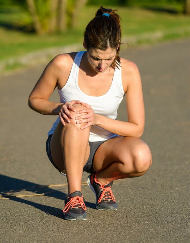 Coureuse accroupie se tenant le genou, gênée par une douleur au tendon pendant une sortie de course à pied