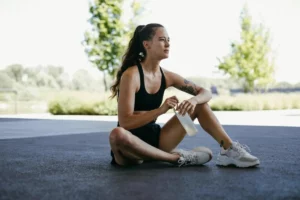 Sportive assise au sol, gourde à la main, en récupération après une séance d'entraînement en extérieur