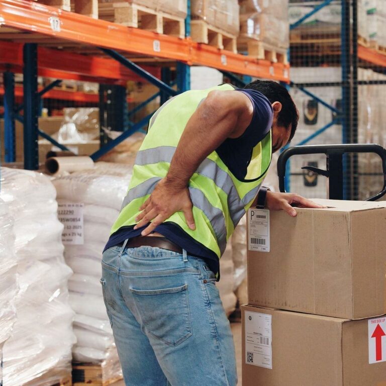 Salarié en entrepôt se tenant le bas du dos, douleur musculosquelettique pendant une manutention